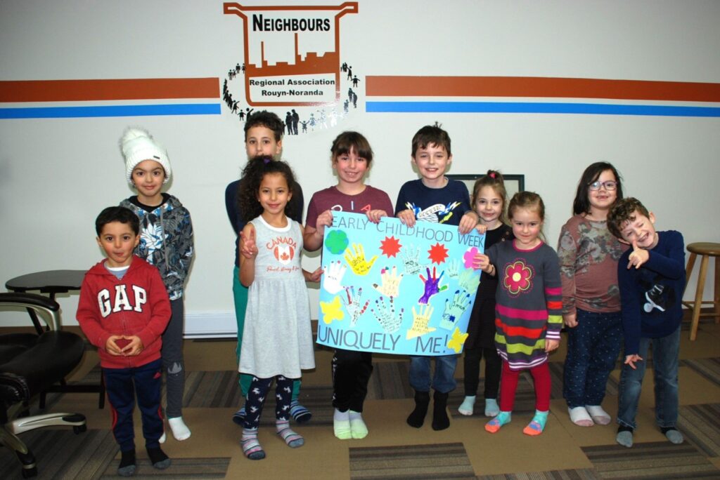 Ten children posing with a hand-made poster that says Early Childhood Week Uniquely Me!