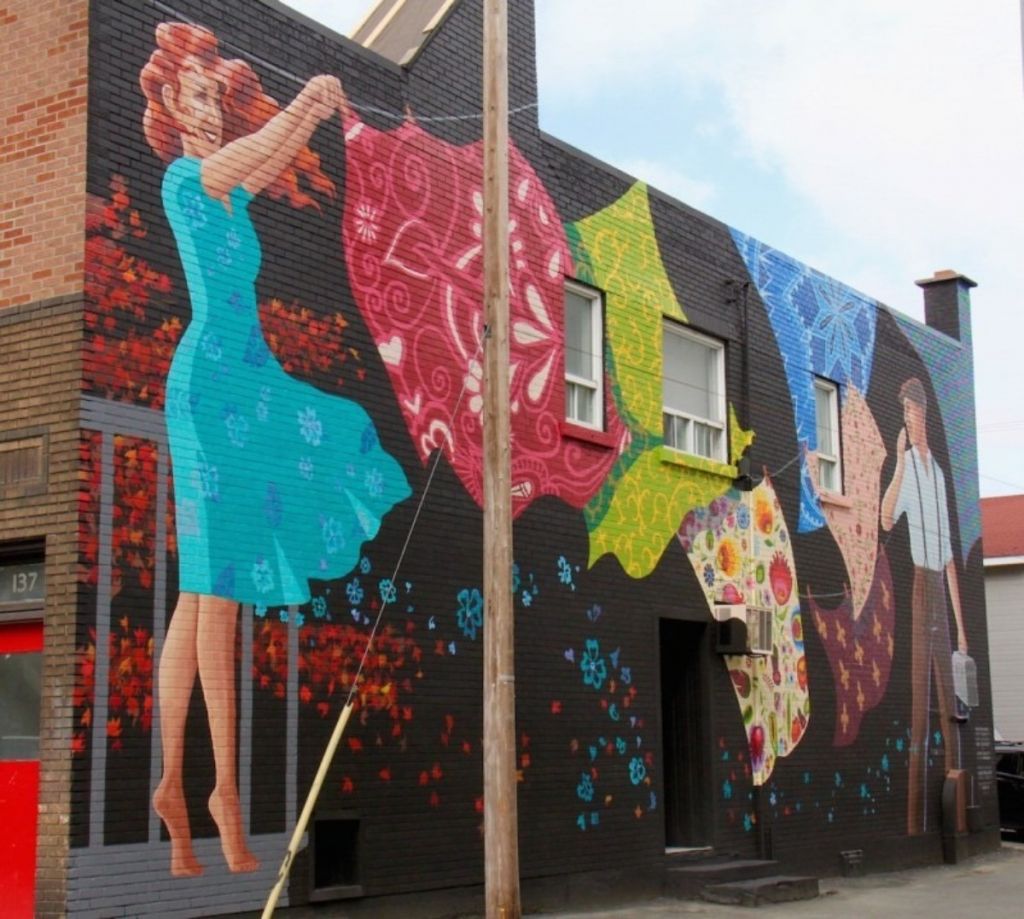 Murale dépeignant une femme accrochant des tissus colorés sur une corde à linge, alors qu'un homme transportant une boîte à lunch l'observe