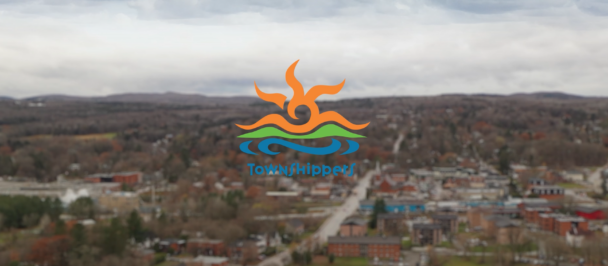 Logo of Townshippers behind a blurred region with plenty of houses and trees